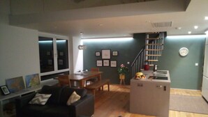 A modern living room with a black sofa, wooden dining table, and a small kitchen area with a fruit bowl. - Exclusive Garden Apartment (Galway)
