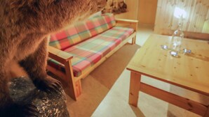 Ein gemütliches Wohnzimmer mit einem karierten Sofa, einem Holztisch und einer Katze, die auf einem Stein sitzt.