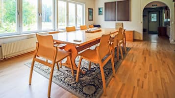 A spacious dining area with a large wooden table and chairs, a patterned rug, and large windows allowing natural light.
