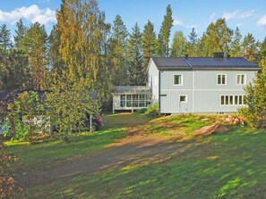 A two-story house with a sloped roof, surrounded by a forested area.