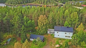 Eine abgelegene Hütte mit einer großen Terrasse, umgeben von dichtem Wald und einem Fluss.