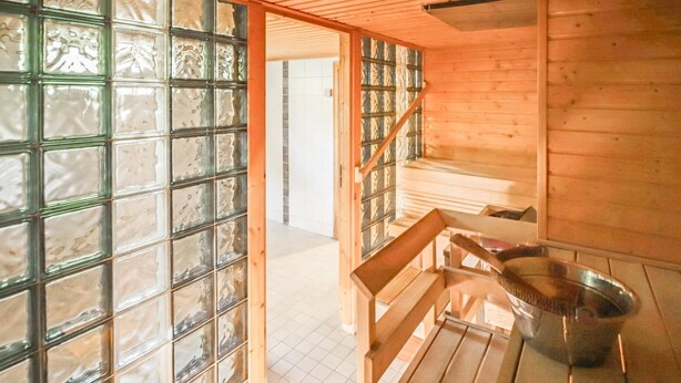 Ein Holzkabine mit einer Bank und einem Metallbecken, vermutlich eine Sauna oder ein Dampfbad.