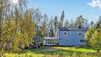 A two-story house with a large windowed extension, surrounded by trees and a well-maintained lawn.