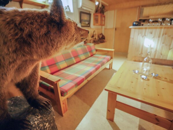 A fox statue in a room with a wooden table, a plaid sofa, and a kitchen area in the background.