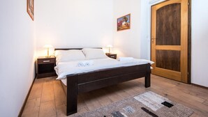 Une chambre à coucher avec un lit en bois, deux tables de chevet avec des lampes, une porte en bois et un petit tableau accroché au mur.