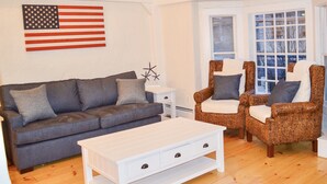 A living room with a gray sofa, two wicker armchairs, a white coffee table, and a white side table. An American flag is mounted on the wall. - Spacious home in the Heart of Downtown Newport! Walk Everywhere  (Newport)