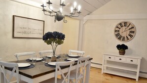 A dining area with a wooden table, white chairs, a chandelier, a wall clock, and a framed quote. - Spacious home in the Heart of Downtown Newport! Walk Everywhere  (Newport)