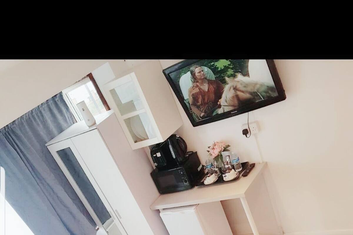 Quarto de hotel com duas camas, uma escrivaninha com cafeteira, televisão e janela com cortinas.