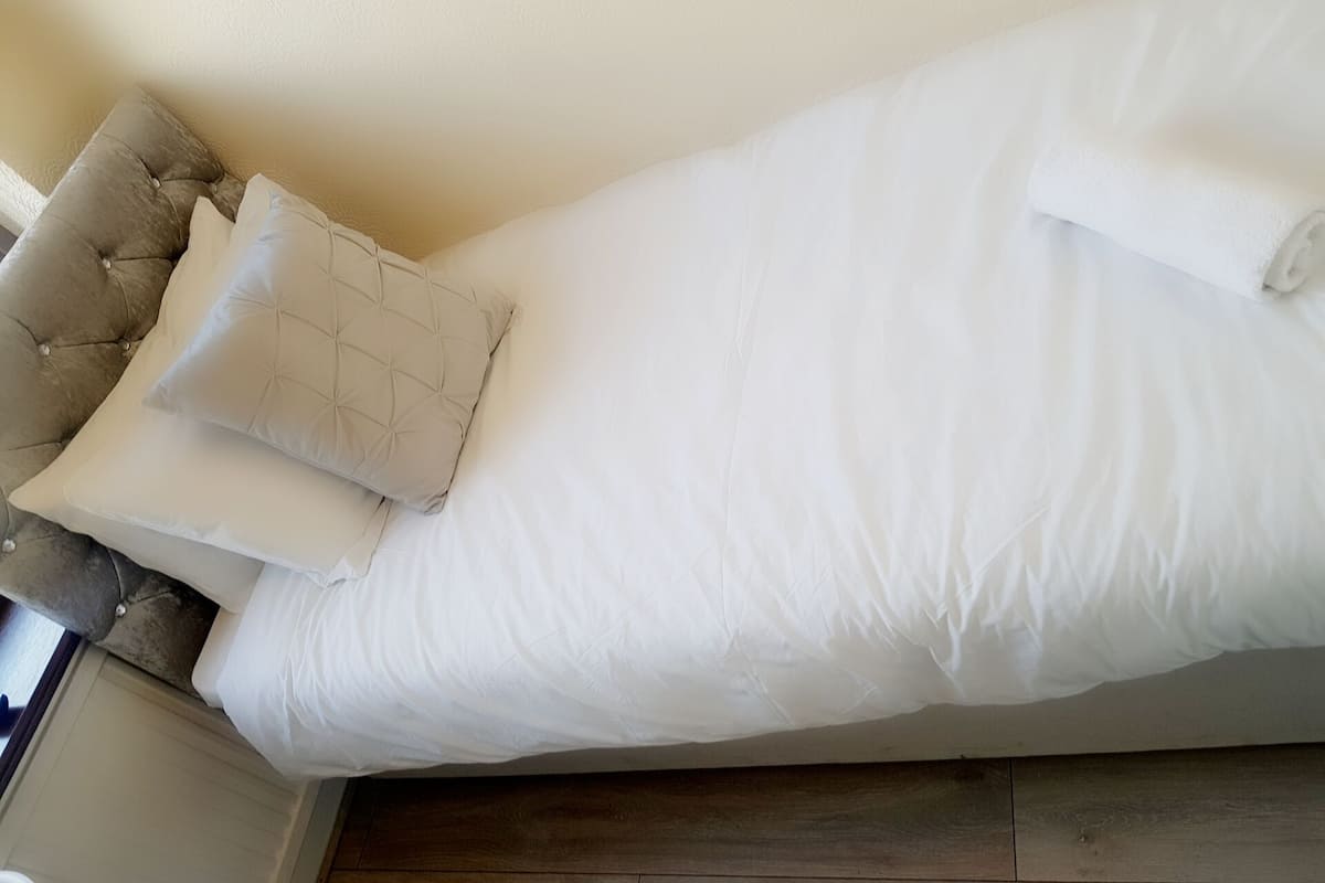 Cama com roupa de cama branca e cabeceira estofada.