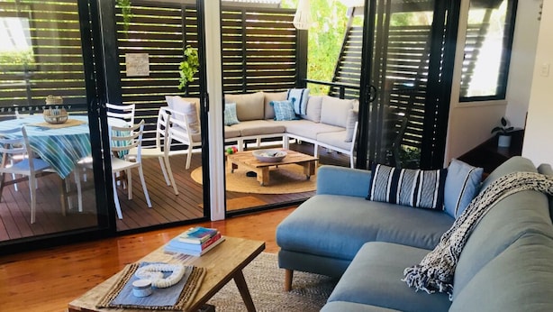 Un salon avec un canapé bleu, une table basse en bois et un coin repas avec une nappe à rayures.
