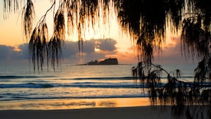 Une scène de plage avec un coucher de soleil, des vagues et une île au loin.