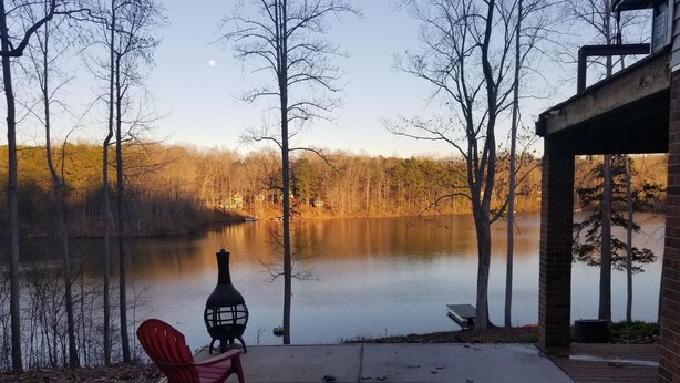 Une terrasse au bord du lac, avec un fauteuil Adirondack rouge, une lanterne décorative et une jetée qui s’avance dans l’eau.
