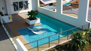 Une piscine intérieure moderne, avec une eau d’un bleu limpide, entourée d’une rambarde en verre, et offrant une vue sur les maisons voisines et les panneaux solaires.