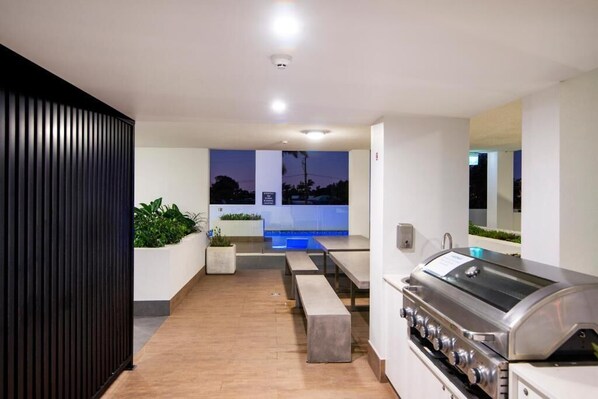 Ein moderner Außenbereich mit Grill, Sitzgelegenheiten und Blick auf einen Pool in der Abenddämmerung.