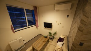 Een woonkamer met een houten salontafel, een beige bank, een aan de muur bevestigde televisie en een raam met uitzicht op een besneeerd landschap.