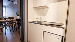 Een compacte keuken met een ingebouwd spoelgedeelte, een kleine koelkast en een eethoek met stoelen en een tafel.