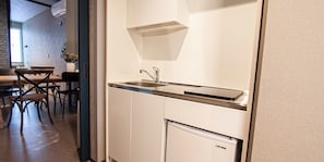 A compact kitchen with a built-in sink, a small refrigerator, and a dining area with chairs and a table. - UCHI SUSUKINO WEST by Hotel Wheat  (Sapporo)