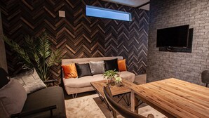 Een moderne woonkamer met een visgraatmotief aan de muur, een bank met meerdere kussens, een houten salontafel en een aan de muur bevestigde televisie.