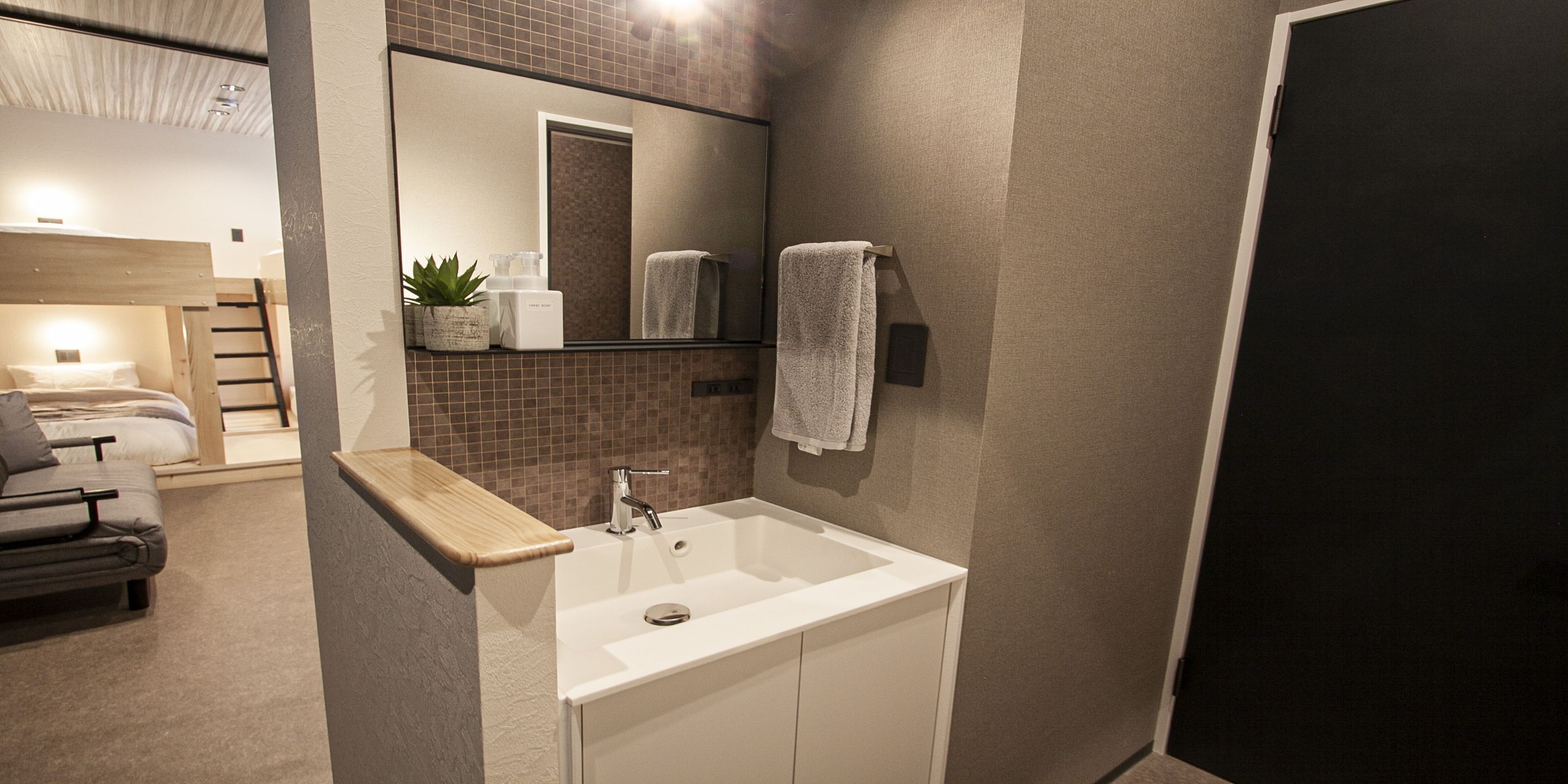 A modern bathroom with a white sink, mirror, and towel rack. There is a wooden bench and a small plant on the counter.