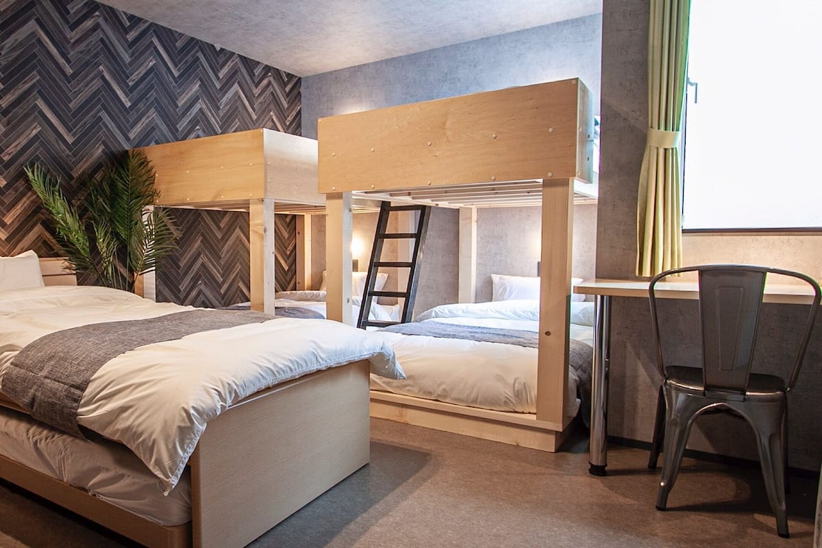 A modern bedroom with a herringbone-patterned wall, a bunk bed, a desk, and a chair.