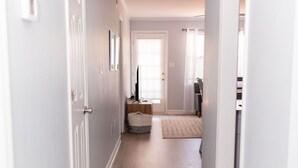 Un pasillo con suelo de madera y paredes blancas que da a una habitación con cama y ventana.