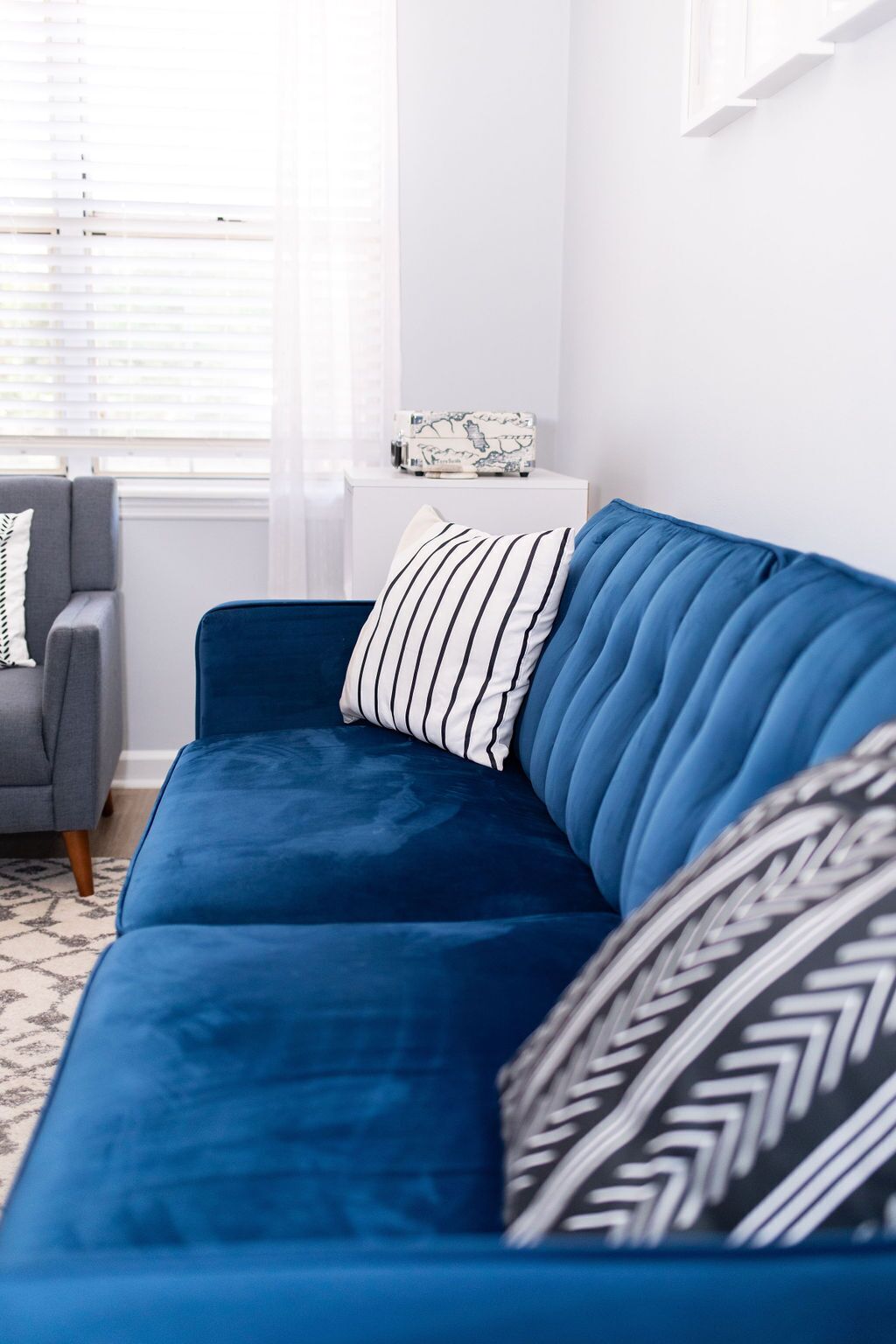 Un canapé bleu agrémenté de coussins à rayures et à motifs, un fauteuil gris et une petite table d’appoint blanche sur laquelle repose une boîte décorative.
