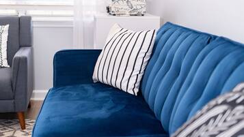Un canapé bleu agrémenté de coussins à rayures et à motifs, un fauteuil gris et une petite table d’appoint blanche sur laquelle repose une boîte décorative.