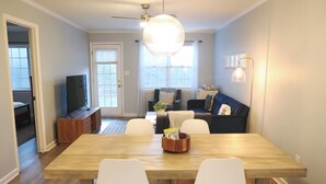 Un comedor con una mesa de madera, sillas blancas, un televisor y un ventilador de techo.