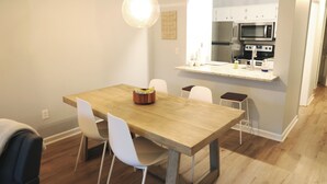 Una cocina moderna con una mesa de comedor de madera, sillas blancas y una lámpara colgante.