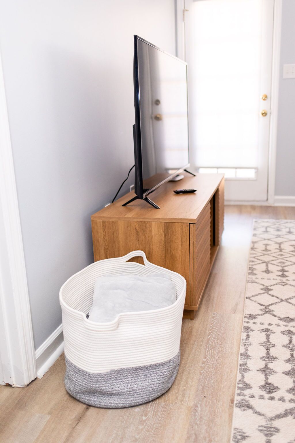 A television on a wooden cabinet, a white basket, and a patterned rug in a hallway.