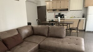 A modern living room with a brown sectional sofa, a dining area with a table and chairs, and a kitchen with cabinets and appliances.