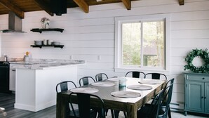A modern kitchen with a wooden ceiling, white walls, and a large island with a dining table and chairs. - Beautiful Lakefront Retreat on Long Lake – Sleeps 11 (BRIDGTON)