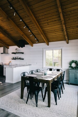 A modern kitchen with a wooden ceiling, white walls, and a large island with a dining table and chairs.