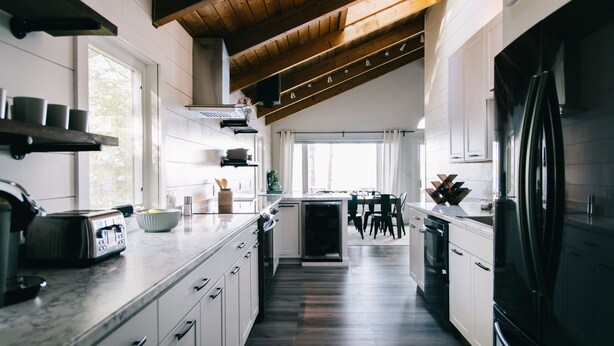 A modern kitchen with white cabinets, a black refrigerator, and a wooden ceiling. - Beautiful Lakefront Retreat on Long Lake – Sleeps 11 (BRIDGTON)