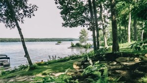 A lakeside view with a stone pathway, lush greenery, and a parked car. - Beautiful Lakefront Retreat on Long Lake – Sleeps 11 (BRIDGTON)