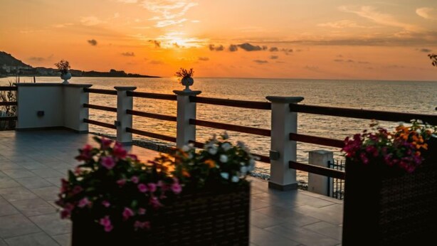 A terrace with a view of the sunset over the sea, railings, and flower planters. - Apartment Nina by Interhome (Marina di Caronia)