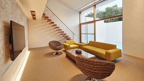 Una sala de estar moderna con un televisor grande, sofás amarillos, una mesa de centro tejida de diseño original y una escalera con escalones de madera.