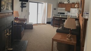 A living room with a fireplace, a television, a ceiling fan, and a kitchen area with a refrigerator and microwave. - Hidden Valley - Walk to Slopes and Pool - 2 BR with Fireplace + WIFI (Hidden Valley)