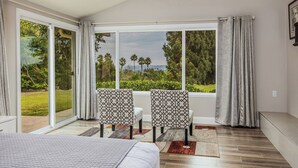 A bedroom with a large sliding glass door leading to a balcony, two patterned chairs, a bed, and a view of greenery and trees. - Rancho Santa Fe Beauty, close to Del Mar Race Track & Riding Club (Rancho Santa Fe)
