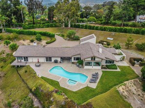 A modern two-story house with a swimming pool, surrounded by well-maintained lawns and trees.