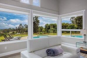 A modern living room with large windows overlooking a pool and garden.