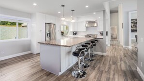 A modern kitchen with a central island, bar stools, stainless steel appliances, and pendant lighting. - Rancho Santa Fe Beauty, close to Del Mar Race Track & Riding Club (Rancho Santa Fe)