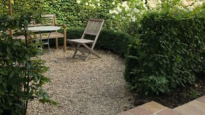 Un espace extérieur aménagé avec une table et des chaises, entouré d’une haie et de différentes espèces de plantes.