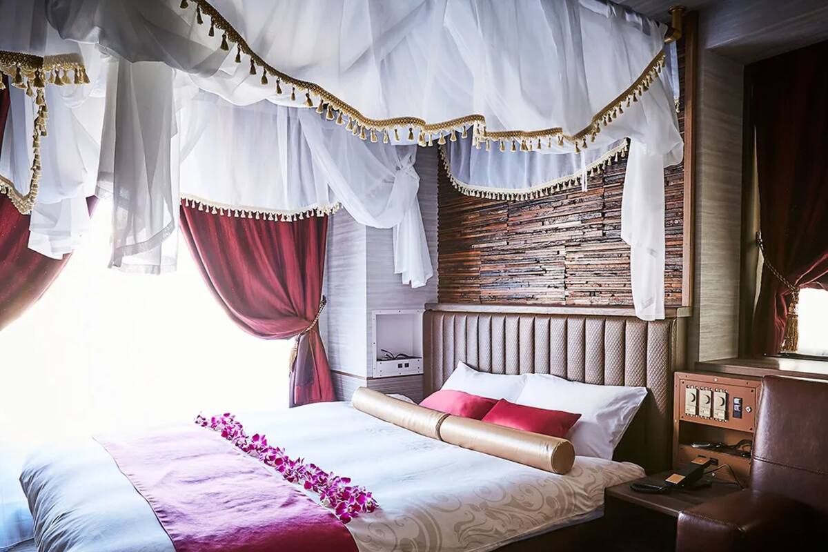 A bedroom with a canopy bed, a headboard with a textured pattern, and a bedside table with a lamp.