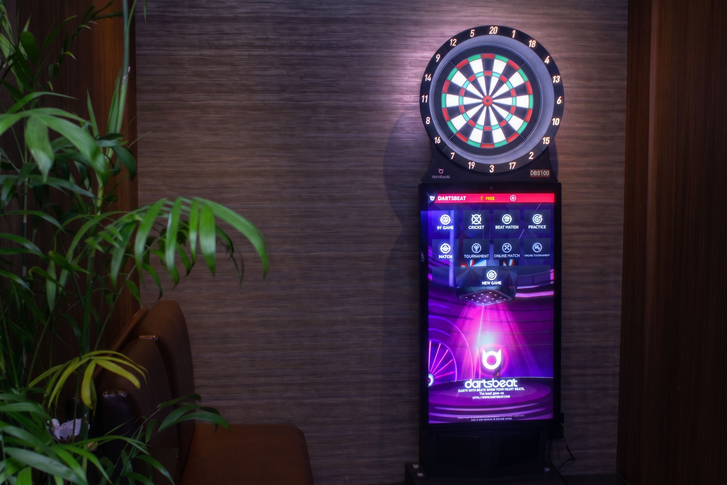 A dartboard with a digital display on a stand, placed against a wooden wall.