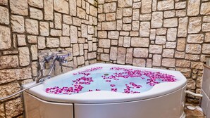 A stone-walled bathroom with a bathtub filled with water and rose petals. - Petit Bali Ikebukuro - Adults Only (Tokyo)
