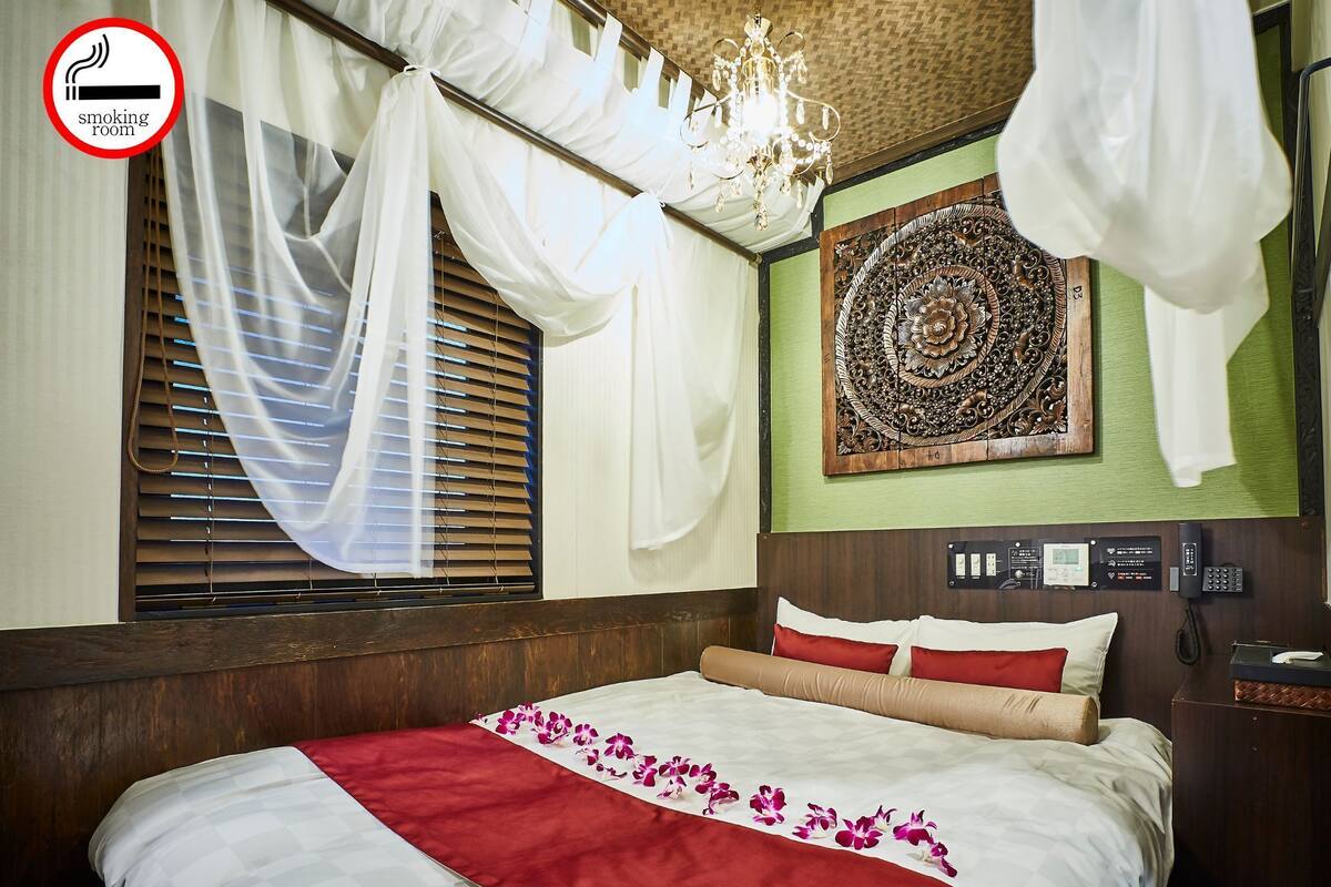A hotel room with a bed, a chandelier, a decorative wall piece, and a sign indicating a smoking room.