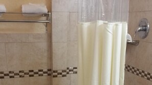 A bathroom with a toilet, a shower with a curtain, and a towel rack. - Palms Inn (Dania Beach)