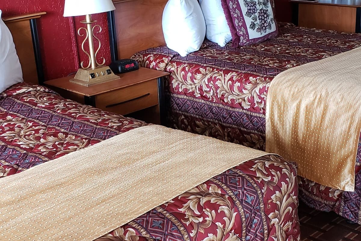 Quarto de hotel com duas camas, cada uma com colcha estampada, cabeceira de madeira e mesa de cabeceira com abajur e controle remoto.