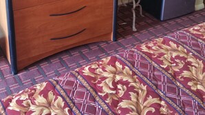 A hotel room with a wooden entertainment unit, a television, a small refrigerator, and a patterned carpet. - Palms Inn (Dania Beach)